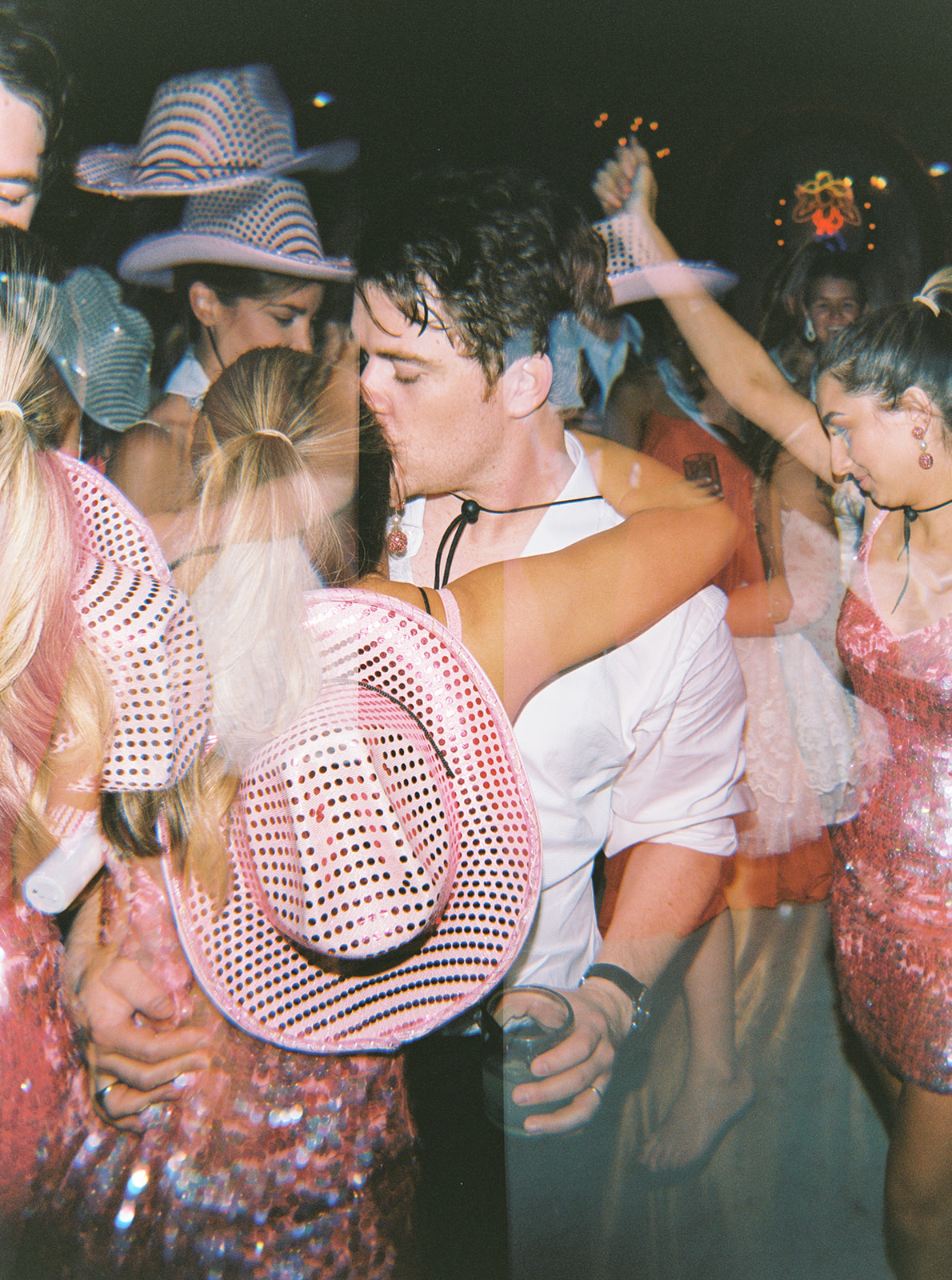 35mm film photo artistically double exposed with a bride and groom kissing on the dance floor overlaid with guests dancing shot with direct flash.