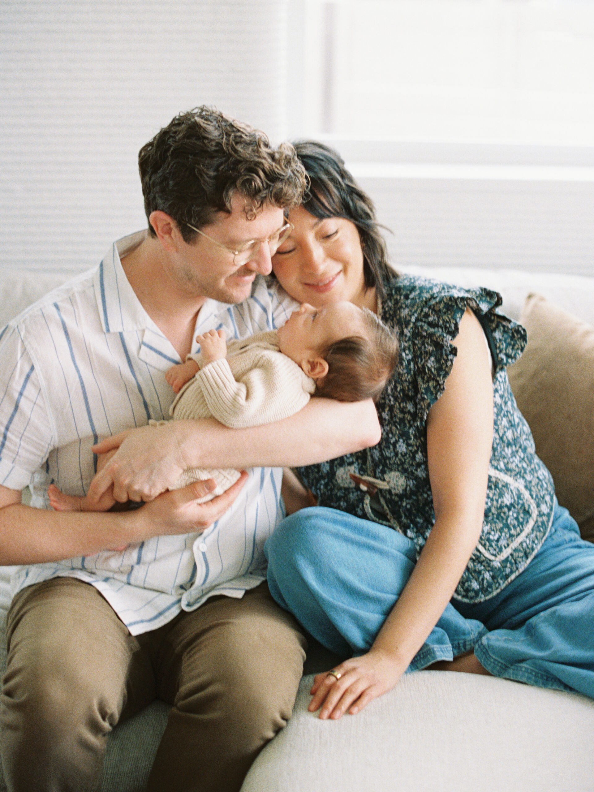 Parents looking lovingly at their newborn on the couch together during an in home newborn session in Austin, TX on film