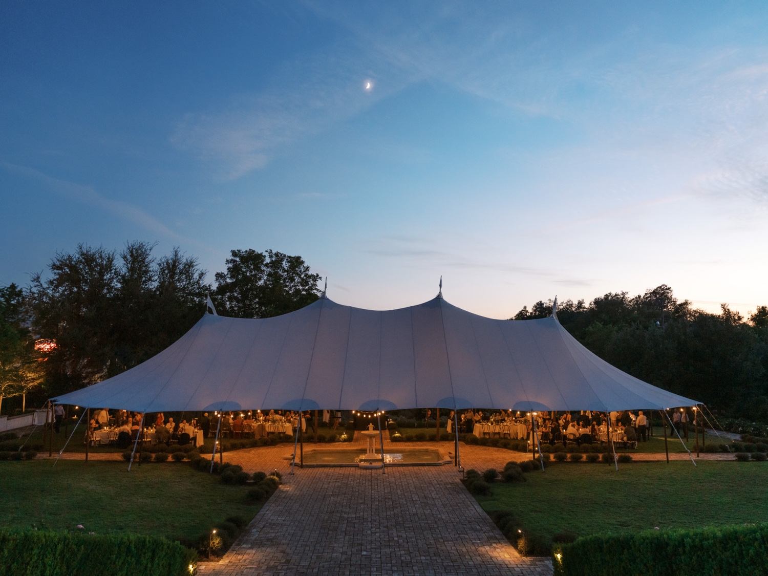 A candlelit reception tent glowing at dusk in the Commodore Perry Estate garden