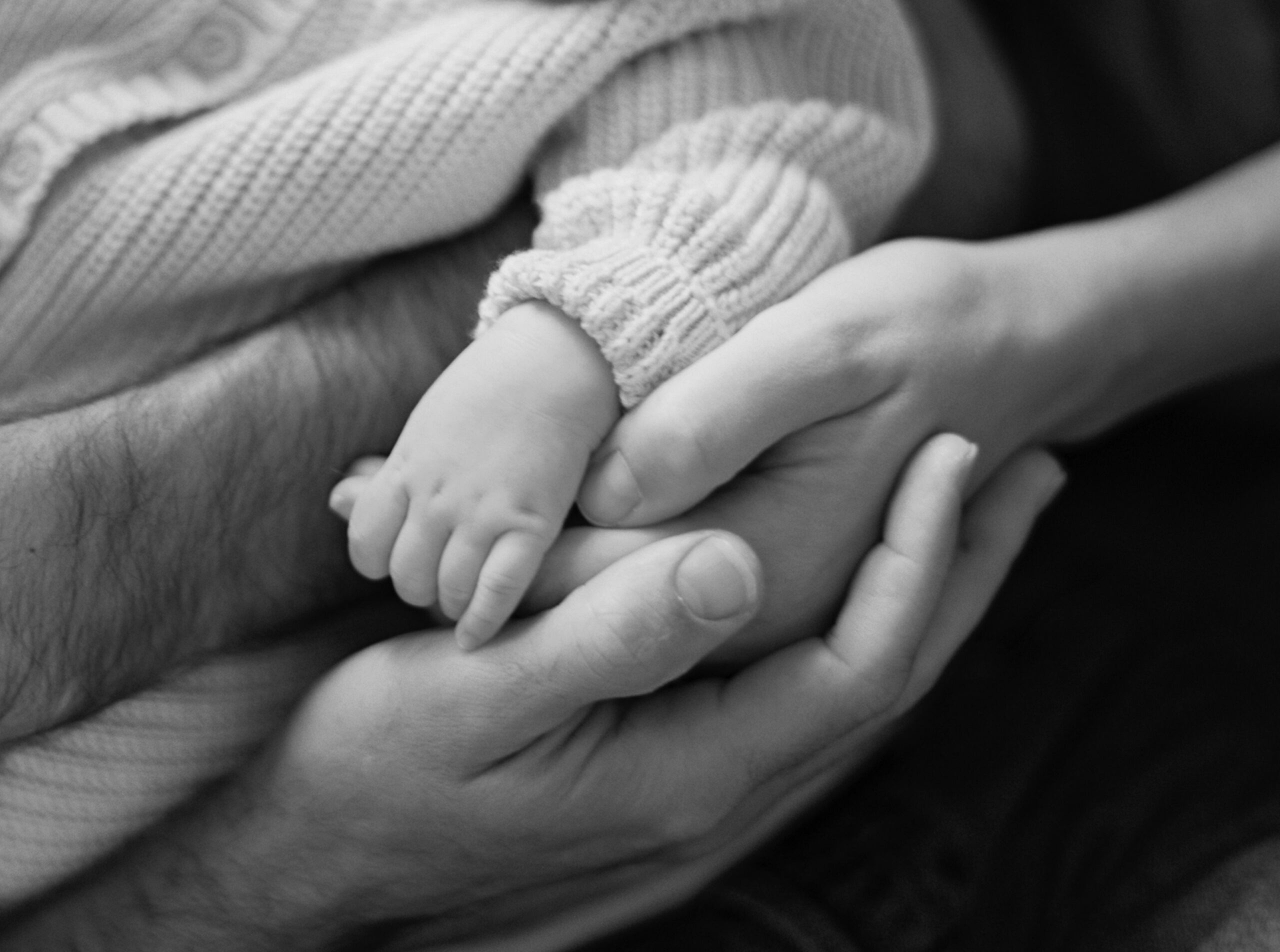 Newborn baby's hand placed in mom's hand with both being held by dad's hand.